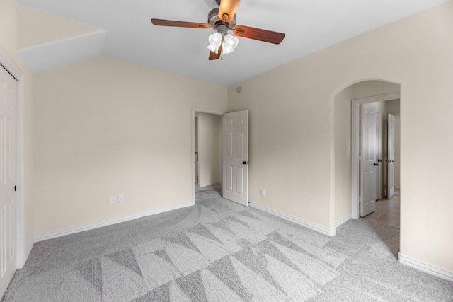 empty room with baseboards, a ceiling fan, arched walkways, and light carpet