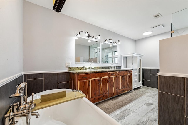 bathroom with double vanity, a tub to relax in, visible vents, wood finished floors, and wainscoting
