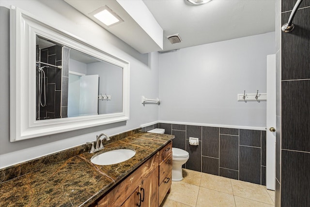 bathroom with tile walls, a wainscoted wall, toilet, vanity, and a shower