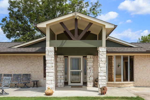 view of exterior entry featuring brick siding and a shingled roof