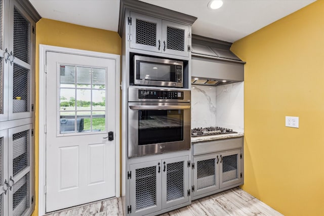 kitchen featuring light wood finished floors, recessed lighting, tasteful backsplash, premium range hood, and appliances with stainless steel finishes