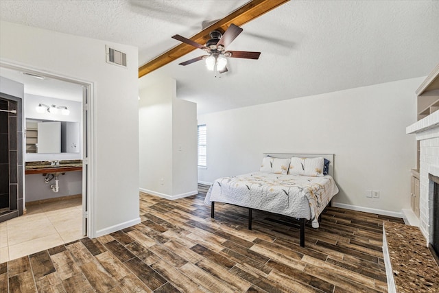 bedroom featuring wood finished floors, visible vents, a textured ceiling, and a brick fireplace