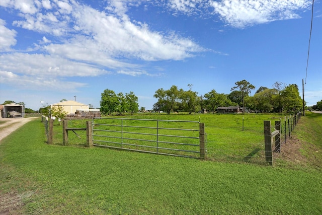 view of gate with fence, a yard, and a rural view