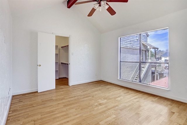 unfurnished bedroom with baseboards, vaulted ceiling with beams, light wood-style flooring, ceiling fan, and a walk in closet