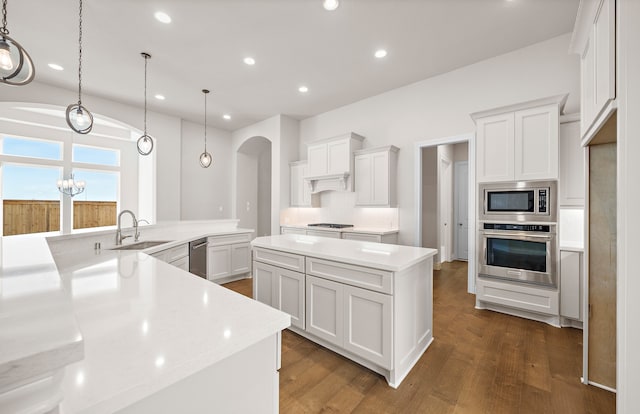 kitchen with a sink, a spacious island, stainless steel appliances, arched walkways, and dark wood-style flooring