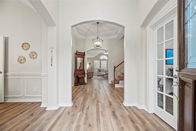foyer featuring arched walkways, a tray ceiling, stairway, and light wood-type flooring