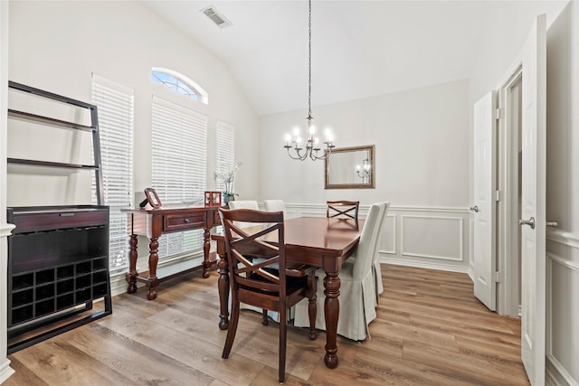 dining room featuring visible vents, wainscoting, vaulted ceiling, and light wood-type flooring