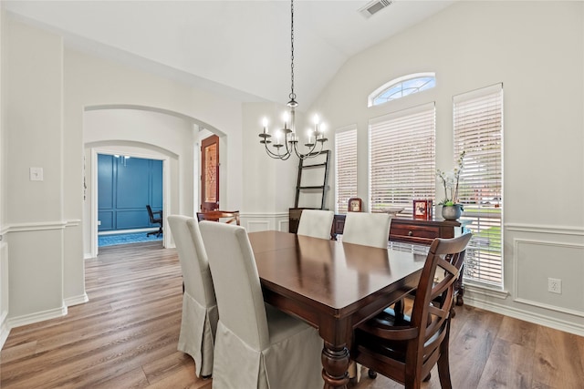 dining room featuring visible vents, a chandelier, arched walkways, light wood finished floors, and vaulted ceiling
