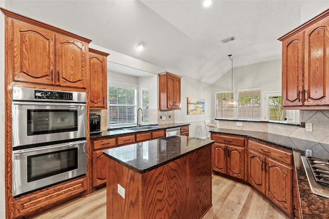 kitchen featuring a sink, appliances with stainless steel finishes, vaulted ceiling, and light wood finished floors