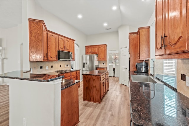 kitchen featuring appliances with stainless steel finishes, a sink, brown cabinetry, dark stone counters, and light wood-type flooring