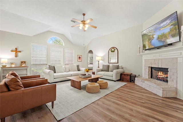 living area featuring ceiling fan, a stone fireplace, wood finished floors, and lofted ceiling