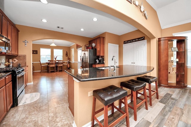kitchen featuring appliances with stainless steel finishes, a sink, arched walkways, a kitchen breakfast bar, and ornamental molding