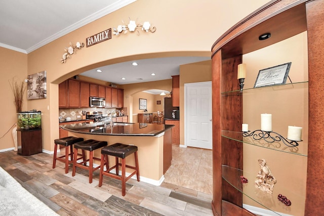kitchen featuring dark countertops, appliances with stainless steel finishes, arched walkways, a kitchen breakfast bar, and ornamental molding