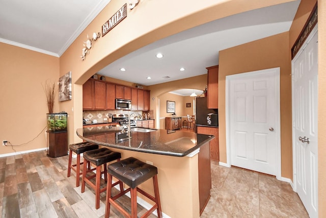 kitchen featuring brown cabinetry, arched walkways, a sink, ornamental molding, and stainless steel appliances