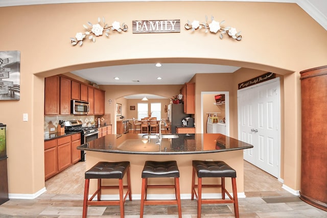 kitchen featuring washer and dryer, appliances with stainless steel finishes, a sink, a breakfast bar area, and arched walkways