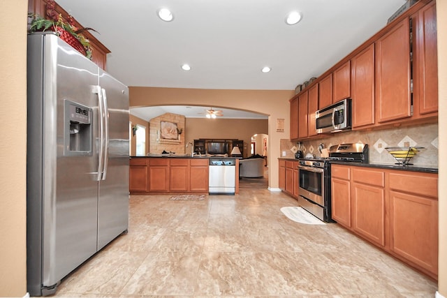 kitchen featuring dark countertops, tasteful backsplash, arched walkways, open floor plan, and stainless steel appliances