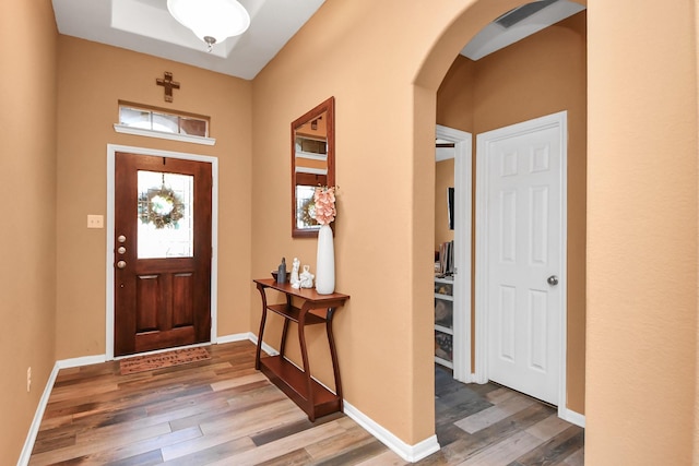 foyer entrance with baseboards, arched walkways, and wood finished floors