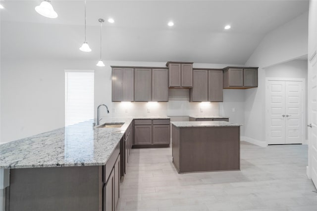 3015 Knotty Forest Dr, Spring, TX 77373 - kitchen with a sink, vaulted ceiling, light stone counters, a center island, and decorative light fixtures