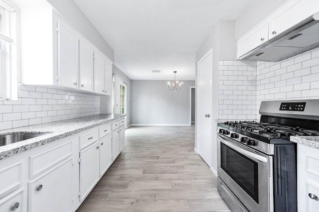kitchen featuring an inviting chandelier, under cabinet range hood, tasteful backsplash, white cabinetry, and gas range