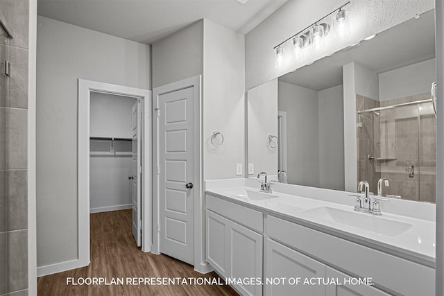 full bath featuring double vanity, a sink, a shower stall, and wood finished floors