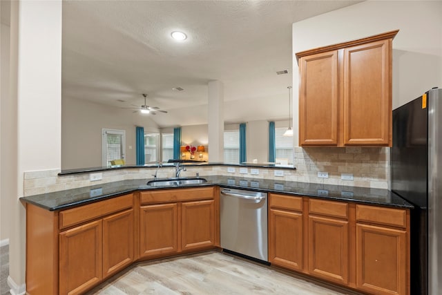 kitchen featuring dark stone counters, a sink, stainless steel appliances, decorative backsplash, and a ceiling fan