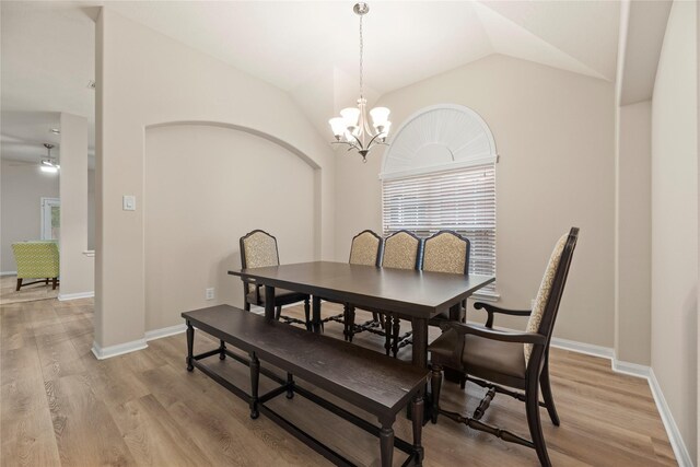 dining room with an inviting chandelier, baseboards, lofted ceiling, and light wood-style floors