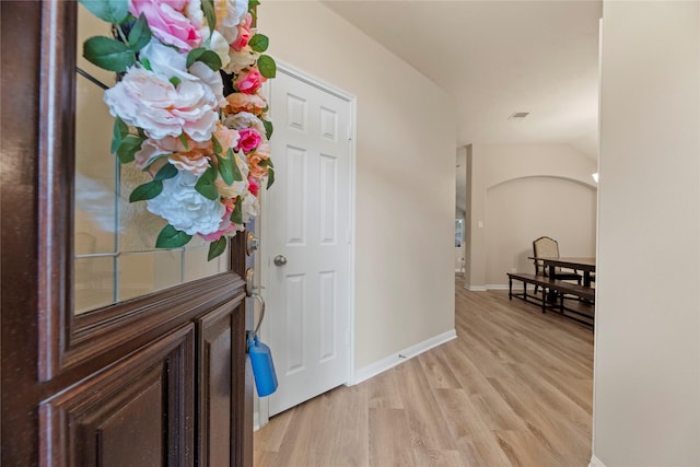 foyer entrance with visible vents, baseboards, vaulted ceiling, and light wood-style floors