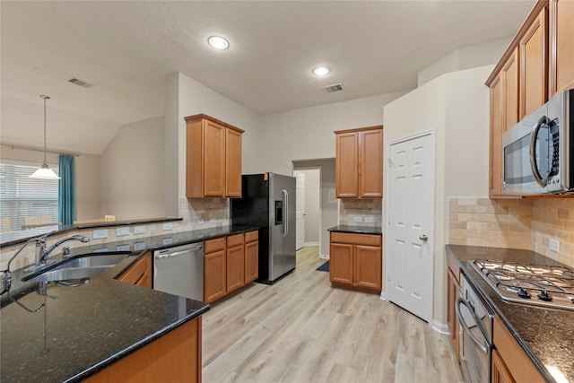 kitchen with appliances with stainless steel finishes, backsplash, light wood finished floors, a sink, and visible vents