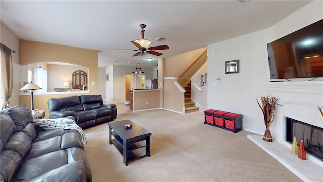 living area featuring stairway, light carpet, ceiling fan, a fireplace, and visible vents