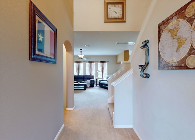 hall with light colored carpet, visible vents, baseboards, and arched walkways