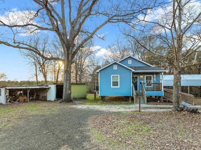 bungalow-style house with covered porch, a shingled roof, an outbuilding, and a pole building