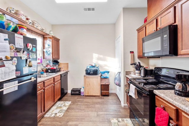 kitchen featuring light wood-style flooring, light countertops, black appliances, a sink, and visible vents