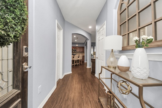 hall with arched walkways, baseboards, and dark wood-type flooring