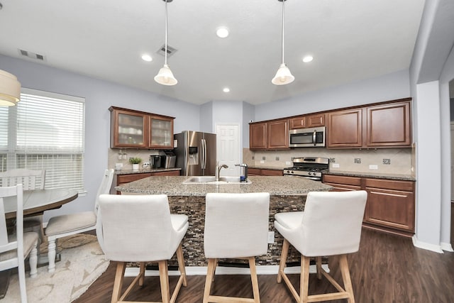 kitchen featuring a sink, visible vents, stainless steel appliances, dark wood-style floors, and a kitchen island with sink