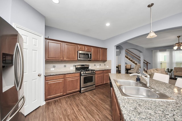 kitchen featuring a sink, ceiling fan, stainless steel appliances, arched walkways, and dark wood finished floors