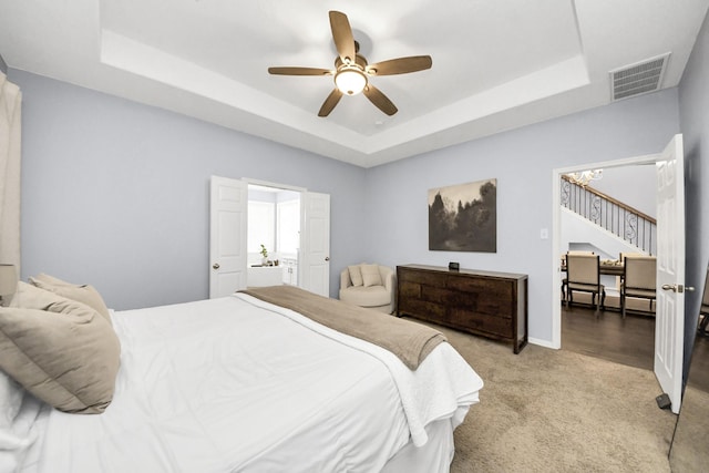 bedroom featuring light colored carpet, baseboards, visible vents, a ceiling fan, and a tray ceiling