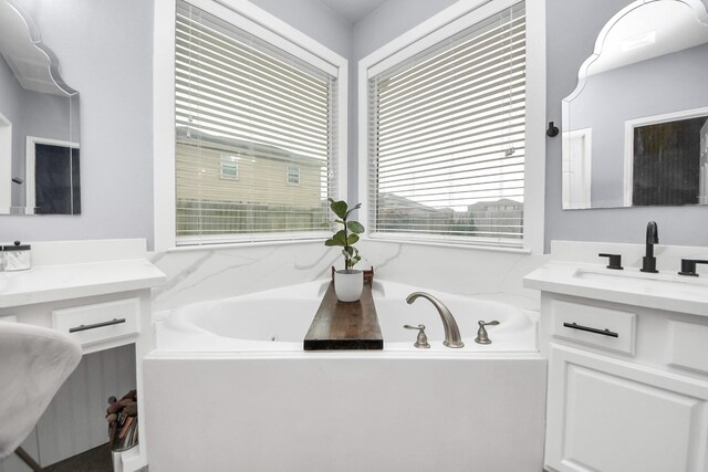 bathroom featuring two vanities, a garden tub, and a sink