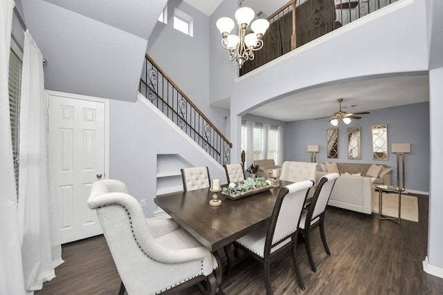 dining space featuring stairway, arched walkways, ceiling fan with notable chandelier, dark wood finished floors, and a high ceiling