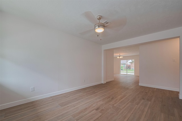 empty room featuring baseboards, ceiling fan with notable chandelier, light wood finished floors, and visible vents