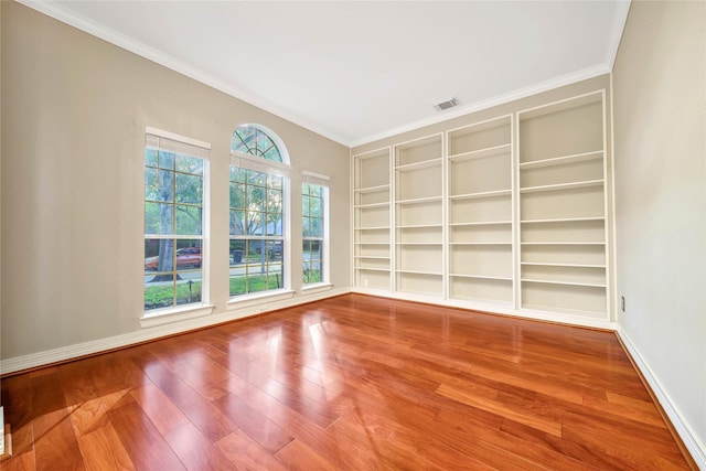 empty room with visible vents, wood finished floors, ornamental molding, and baseboards