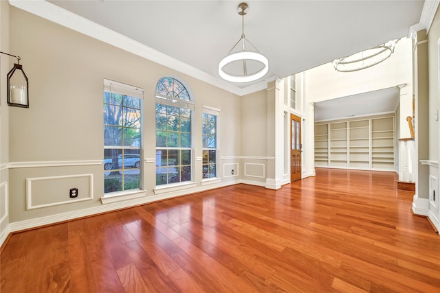 unfurnished dining area featuring wood finished floors, a wainscoted wall, crown molding, and a decorative wall