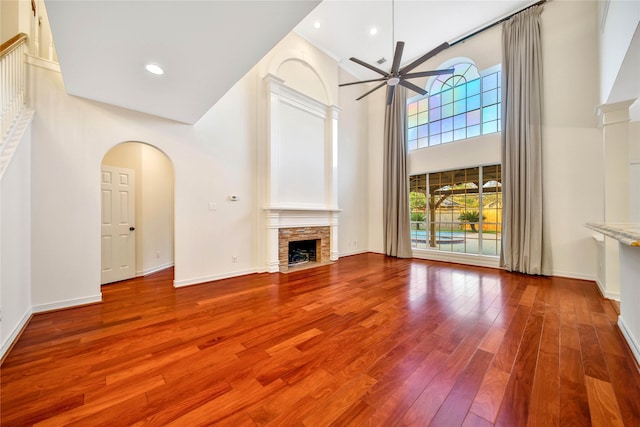 unfurnished living room featuring ceiling fan, arched walkways, a fireplace, wood finished floors, and a high ceiling