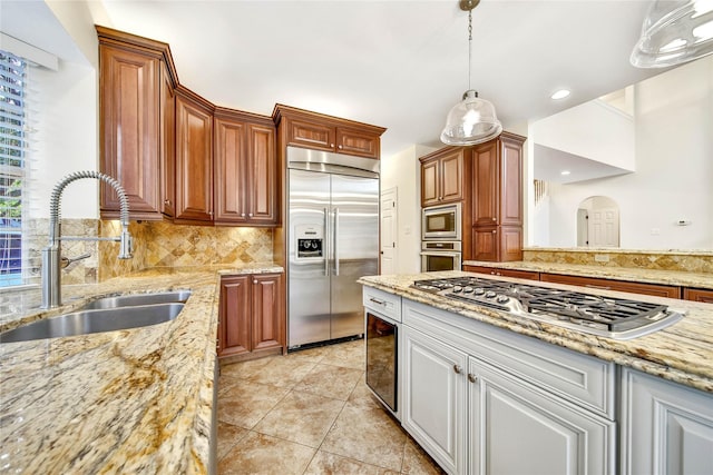 kitchen with light stone counters, pendant lighting, decorative backsplash, a sink, and built in appliances
