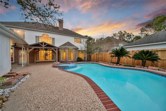 pool at dusk with a patio area, a pool with connected hot tub, and a fenced backyard