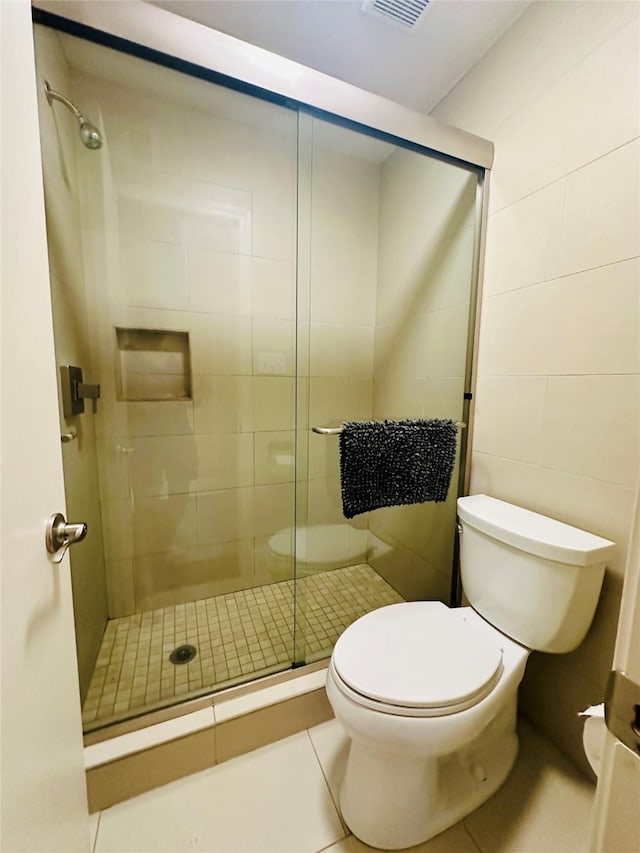 bathroom featuring tile patterned floors, a shower stall, tile walls, toilet, and visible vents