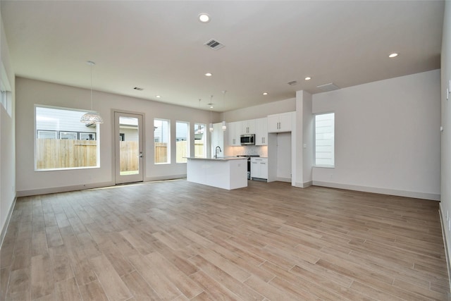 unfurnished living room featuring recessed lighting, a sink, visible vents, light wood-style flooring, and baseboards