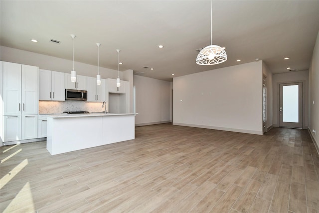 kitchen featuring decorative backsplash, stainless steel microwave, light wood-type flooring, white cabinetry, and visible vents