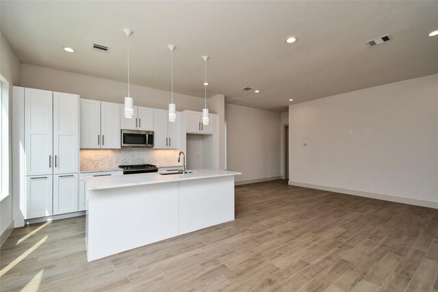 kitchen featuring stainless steel microwave, a sink, tasteful backsplash, visible vents, and an island with sink