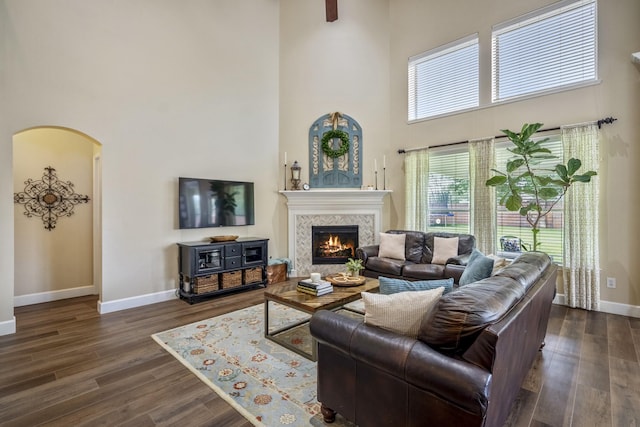 living area featuring a high ceiling, a tile fireplace, dark wood-style floors, baseboards, and arched walkways