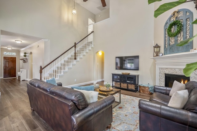 living room with stairs, wood finished floors, a tile fireplace, ceiling fan, and ornamental molding